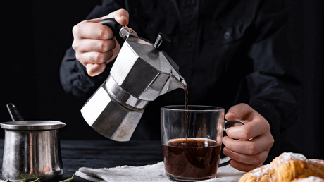 a man pouring coffee from a percolator into a clear glass mug