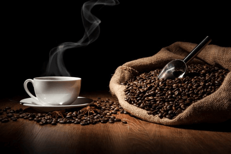a steaming cup of coffee in a white mug surrounded by roasted coffee beans