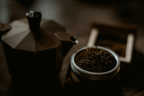 a silver moka pot beside a jar of coffee grounds