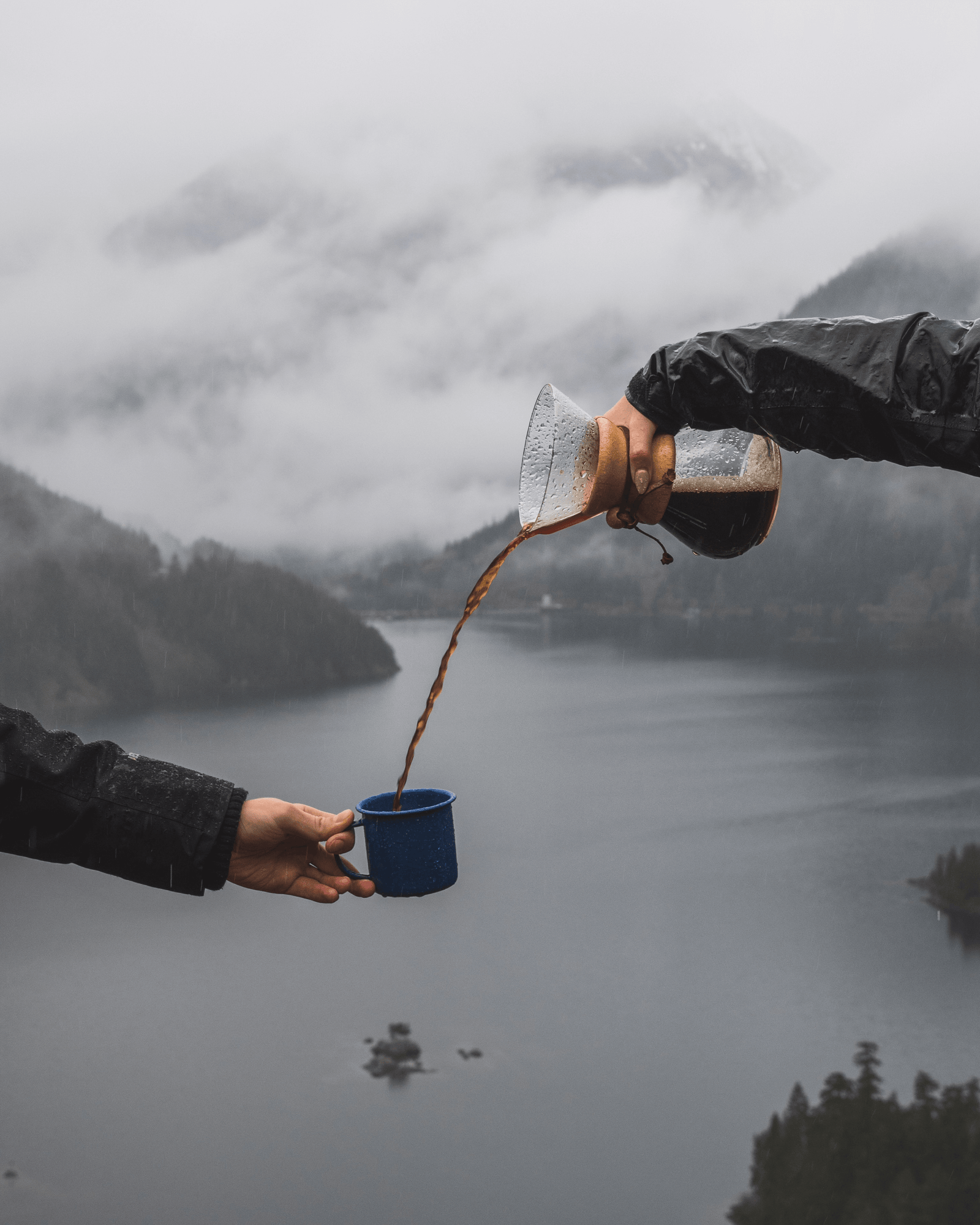 a person pours coffee from a Chemex in to a mug being held by another person